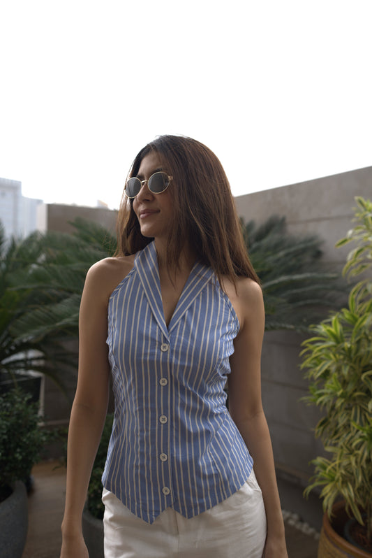 Woman wearing a blue and white striped vest (Talia Vest) with sunglasses, standing in a reflective surface with plants.