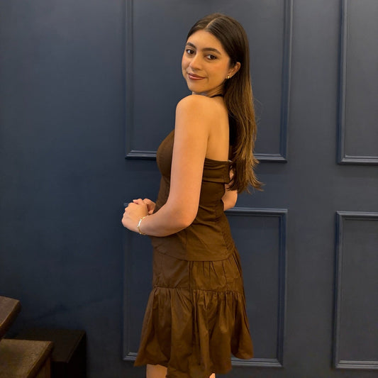 Woman in a brown dress standing against a dark blue paneled wall.